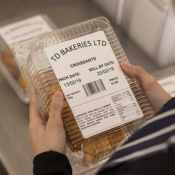 Woman wearing blue and white striped apron holding plastic bakery product with label