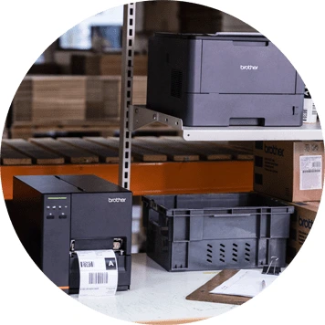 Dark grey Brother printer and label printer on bench, clipboard, paper, racking, boxes