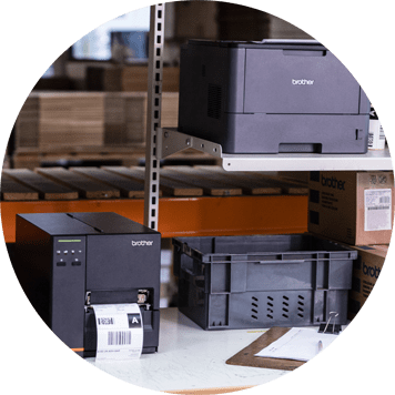 Dark grey Brother printer and label printer on bench, clipboard, paper, racking, boxes