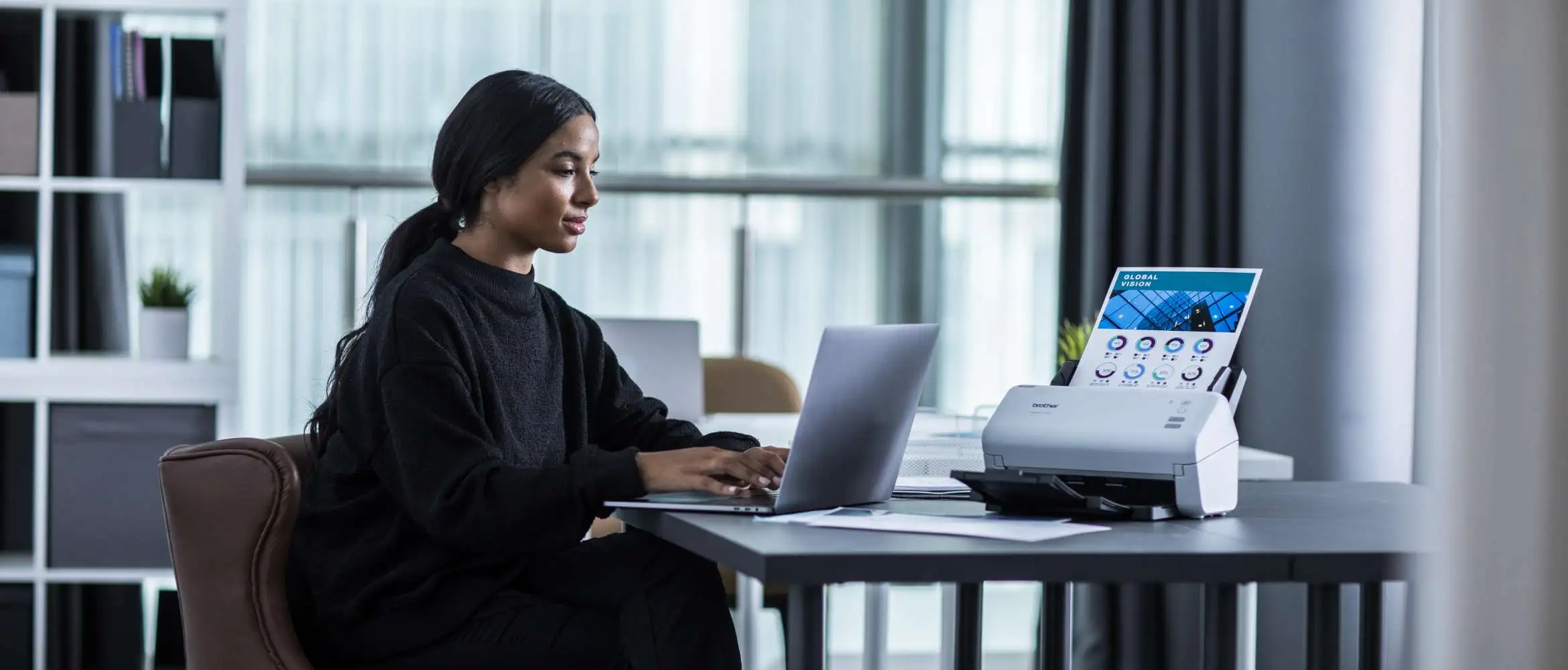 Een vrouwelijke juriste zit aan een bureau op haar laptop te werken met een Brother ADS documentscanner aan haar zijde