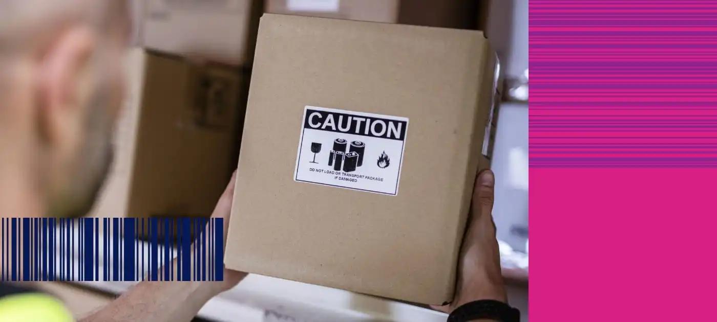 A warehouse worker lifting a brown cardboard box with a black and white caution label off a shelf