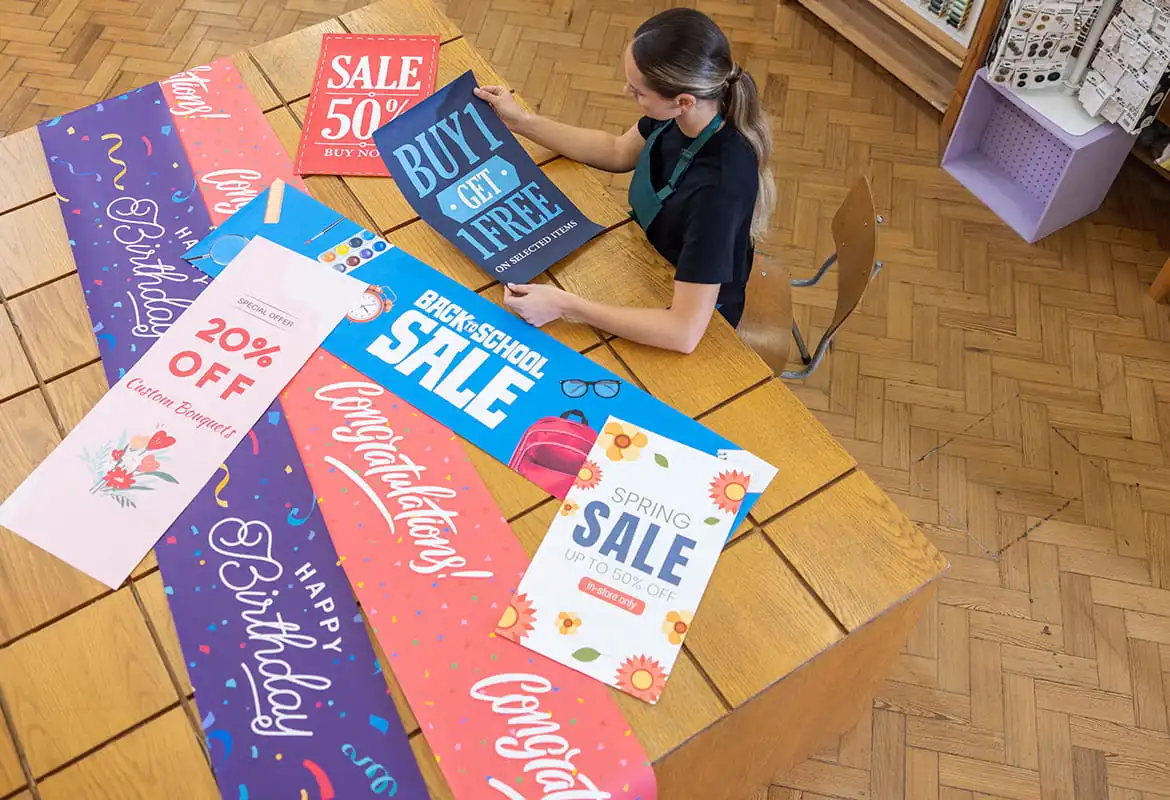 A range of larger format banners on a wooden table, female using laptop